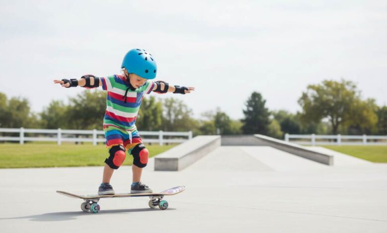 Young child balancing on a colorful beginner skateboard in a park with safety helmet and pads